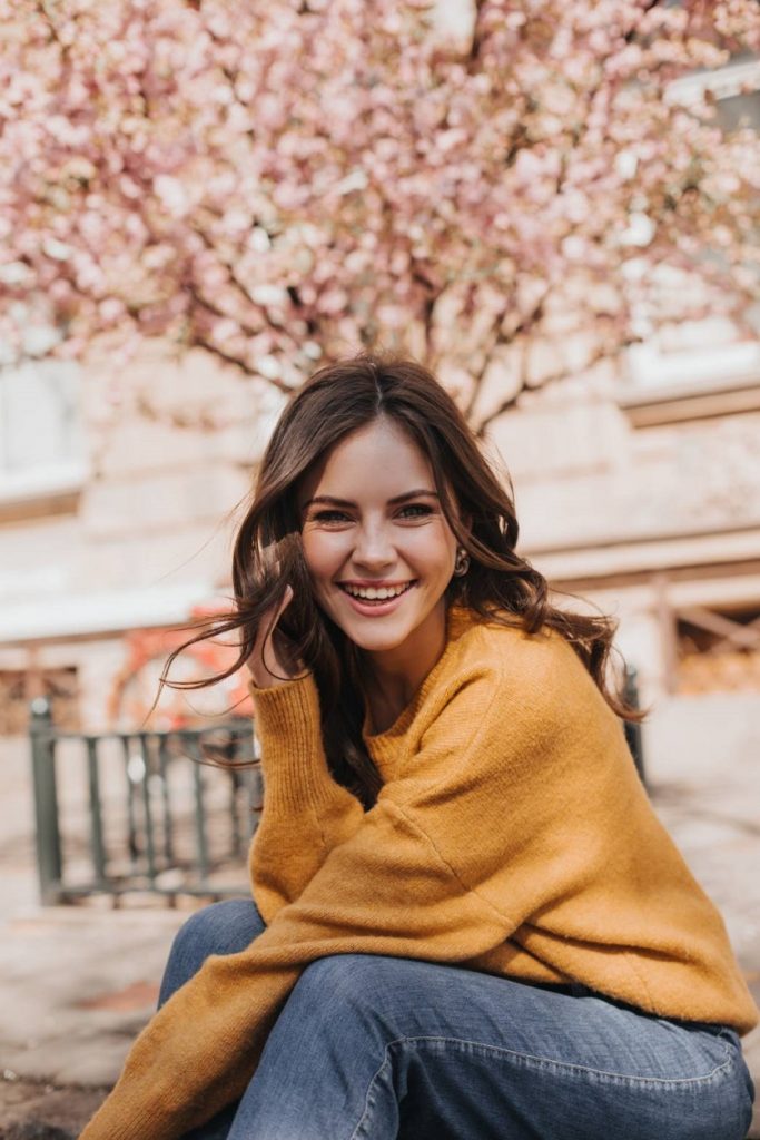 woman sitting and smiling while look at camera with cherry blossom tree in the back ground 