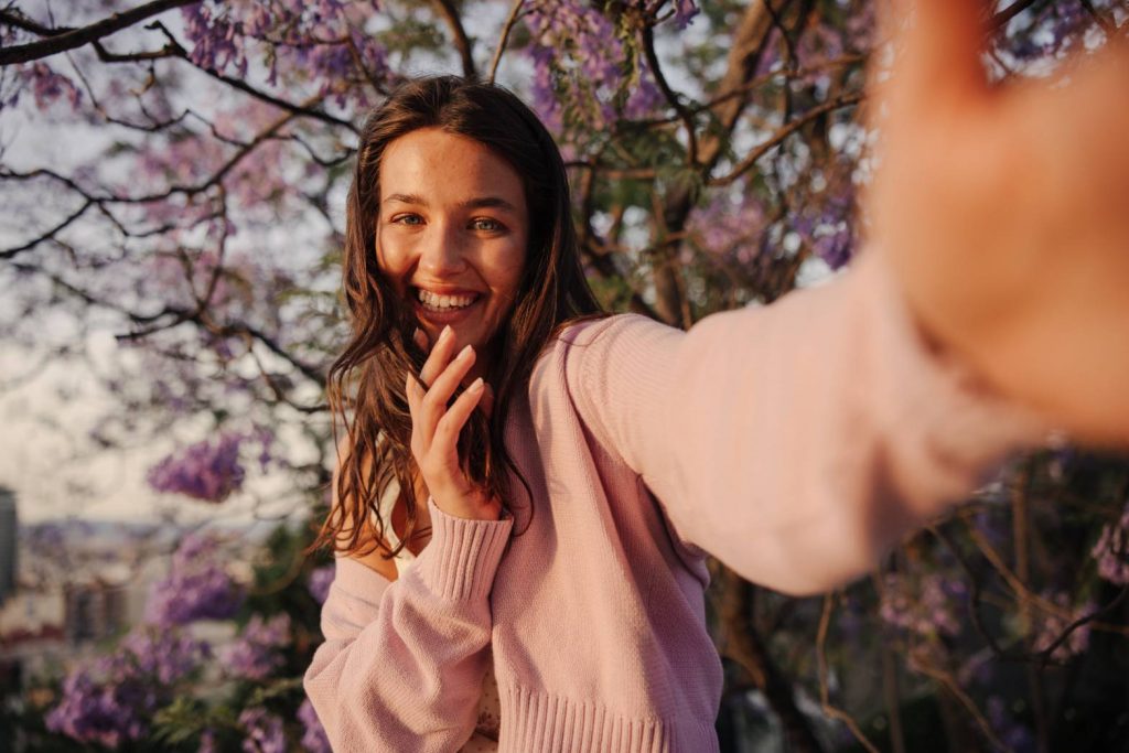 woman pose with hand touching camera and cherry blossom in the background